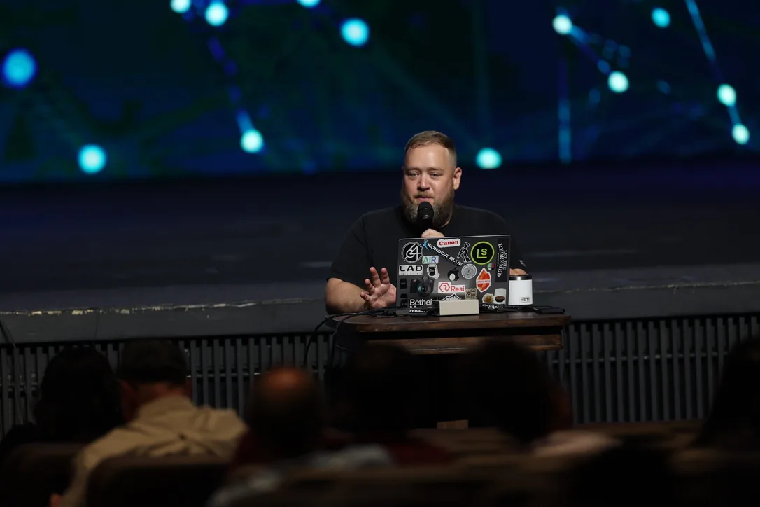 Jesse Maitland teaching from a desk on a dark stage